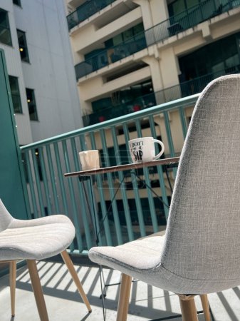 Foto de Vista de ángulo bajo de las tazas de café en la mesa por barandilla y sillas grises vacías en el balcón en el día soleado - Imagen libre de derechos
