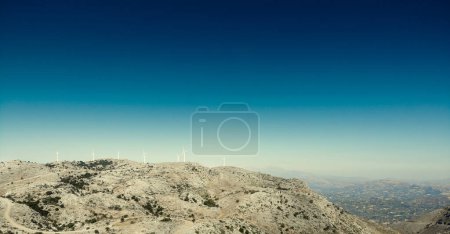 Foto de Vista lejana de las turbinas eólicas en la montaña y vista panorámica del paisaje contra el cielo azul durante el día soleado - Imagen libre de derechos