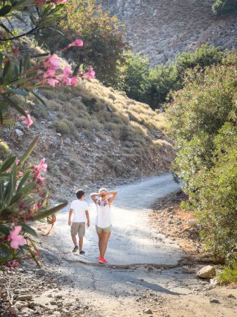 Téléchargez les photos : Vue arrière de la mère et du fils caucasiens marchant sur la route de terre au milieu des plantes tout en profitant des vacances - en image libre de droit