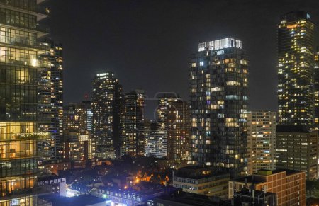 Foto de Vista aérea de rascacielos modernos iluminados con horizonte contra el cielo despejado en la ciudad por la noche - Imagen libre de derechos