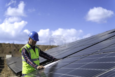 Téléchargez les photos : Portrait de l'ingénieur gestionnaire masculin dans la vérification du casque de sécurité avec un plan un fonctionnement du système de panneaux solaires à la station solaire - en image libre de droit