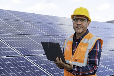 Foto de Retrato del ingeniero gerente masculino en la comprobación del casco de seguridad con el ordenador una operación del sistema del panel solar en la estación solar - Imagen libre de derechos
