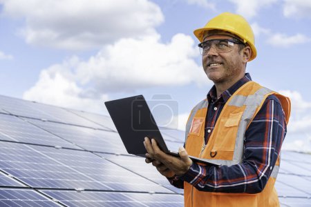 Foto de Retrato del ingeniero gerente masculino en la comprobación del casco de seguridad con el ordenador una operación del sistema del panel solar en la estación solar - Imagen libre de derechos