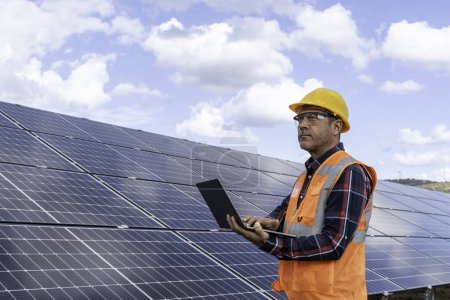 Téléchargez les photos : Portrait de l'ingénieur gestionnaire masculin dans la vérification du casque de sécurité avec ordinateur un fonctionnement du système de panneaux solaires à la station solaire - en image libre de droit