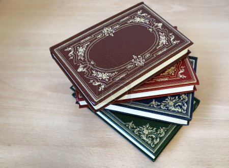 Vintage-Bücher in verschiedenen Farben des Einbands mit goldener Dekoration auf dem Schreibtisch gestapelt