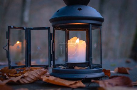 Lantern with burning candle on the table in the evening autumn forest