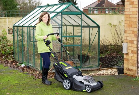 Photo for Capturing an attractive brunette with a new battery operated lawnmower.  These are substantially cheaper if purchased during December, for Christmas, as opposed to March, ready to use in Spring. - Royalty Free Image