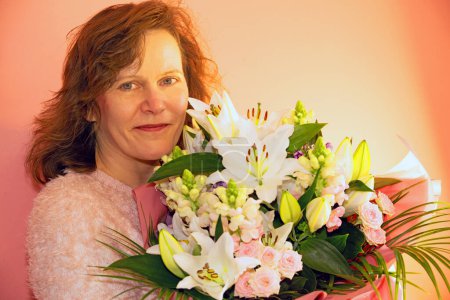 An attractive and mature brunette lady smiling upon receipt of a large bouquet of flowers, on a special occasion.