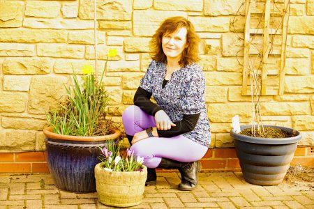 A glamourous brunette lady is pictured proudly squatting beside potted bulbs just coming into flower in early March.