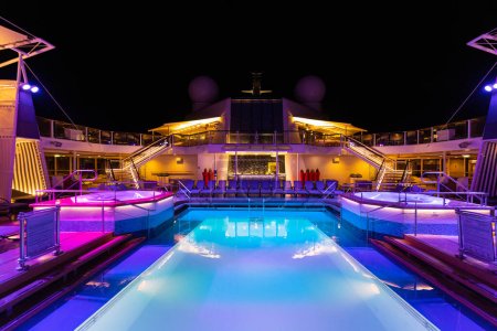 Cruise ship luxury swimming pool at night on top deck with scenic views and entertainment areas.