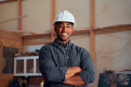 Photo for Portrait of happy multiracial young man in safety helmet looking at camera with arms crossed at woodworking factory - Royalty Free Image