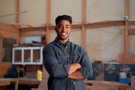 Photo for Portrait of happy multiracial young man in shirt looking at camera with arms crossed at woodworking factory - Royalty Free Image