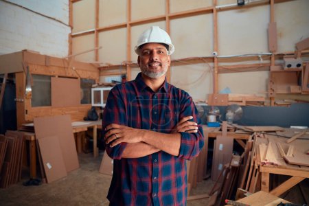 Photo for Portrait of multiracial mid adult man in safety helmet smiling with arms crossed in woodworking factory - Royalty Free Image