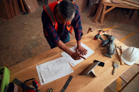 Photo pour Homme adulte moyen multiracial pointant tout en travaillant à côté de la tablette numérique et des outils dans l'usine de travail du bois - image libre de droit