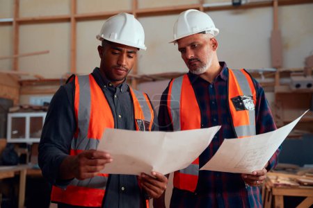 Photo pour Hommes multiraciaux portant un casque de sécurité et des vêtements réfléchissants examinant le papier à l'usine de travail du bois - image libre de droit