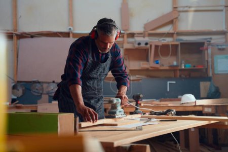 Photo pour Multiracial mi-adulte homme travaillant avec des outils électriques et du bois sur la table dans l'usine de travail du bois - image libre de droit