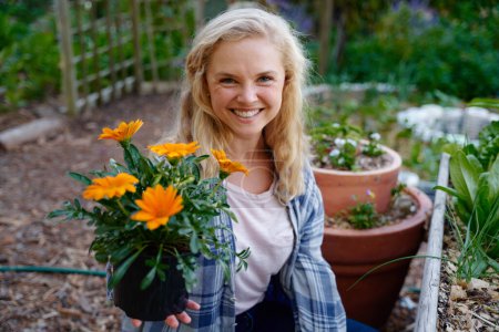 Photo for Happy young caucasian woman looking at camera and smiling while holding flowers at garden center - Royalty Free Image