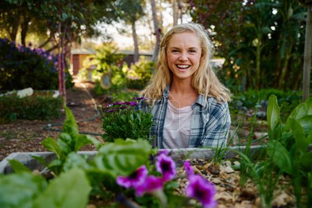 Photo for Happy young caucasian woman in checked shirt looking at camera and smiling by flowers in plant nursery - Royalty Free Image
