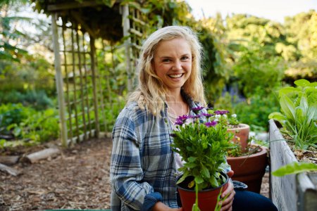Téléchargez les photos : Happy young caucasian woman in checked shirt looking at camera while holding flowers in plant nursery - en image libre de droit