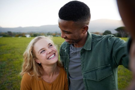 Photo for Happy young multiracial couple in casual clothing smiling while looking at each other in field - Royalty Free Image