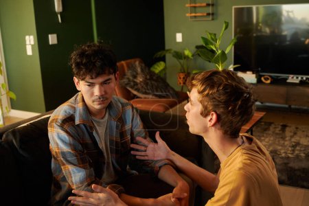 Foto de Frustrated young gay couple wearing casual clothing arguing and gesturing in living room at home - Imagen libre de derechos