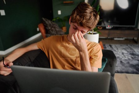 Téléchargez les photos : Frustrated young caucasian man with eyes closed holding eyeglasses by laptop on sofa in living room at home - en image libre de droit
