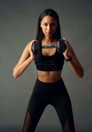 Foto de Mujer biracial joven con confianza que usa sujetador deportivo y polainas con pesas en el estudio - Imagen libre de derechos