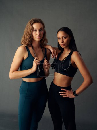 Téléchargez les photos : Determined young woman wearing sports bra holding jump rope while looking at camera with friend - en image libre de droit