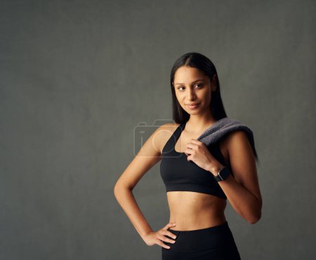 Téléchargez les photos : Jeune femme biraciale portant soutien-gorge de sport et fitness tracker regardant loin tout en tenant une serviette en studio - en image libre de droit