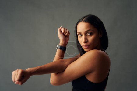 Foto de Retrato de una joven birracial con sujetador deportivo mirando hacia otro lado mientras hace estiramiento de brazos cruzados en el estudio - Imagen libre de derechos