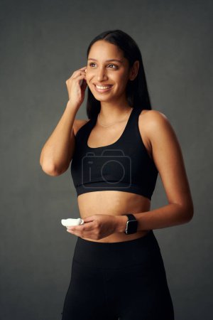 Téléchargez les photos : Biracial jeune femme portant des vêtements de sport souriant tout en tenant sans fil écouteurs intra-auriculaires - en image libre de droit