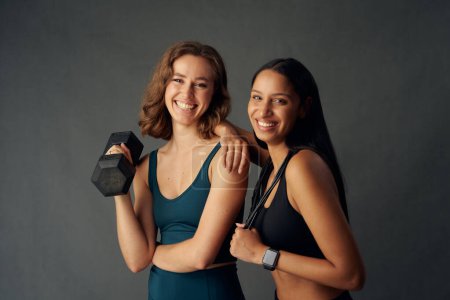 Téléchargez les photos : Young women wearing sports clothing smiling while looking at camera and holding exercise equipment - en image libre de droit