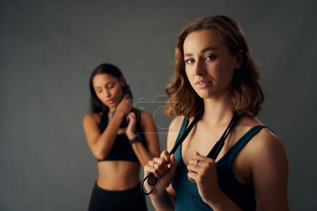 Foto de Mujeres jóvenes confiadas que usan ropa deportiva sosteniendo la cuerda de salto sobre el hombro mientras miran la cámara - Imagen libre de derechos