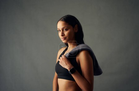 Foto de Retrato de una joven birracial en sujetador deportivo y rastreador de fitness sosteniendo la toalla en el estudio - Imagen libre de derechos