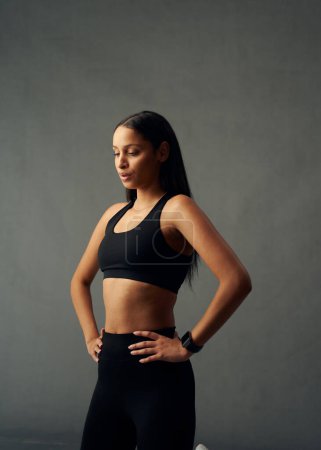 Téléchargez les photos : Young biracial woman wearing sports clothing and fitness tracker exhaling with hands on hips in studio - en image libre de droit