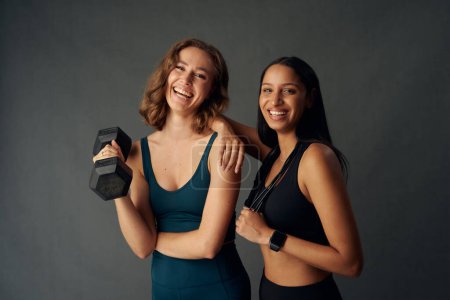 Téléchargez les photos : Young women wearing sports clothing smiling while looking at camera and holding dumbbell - en image libre de droit
