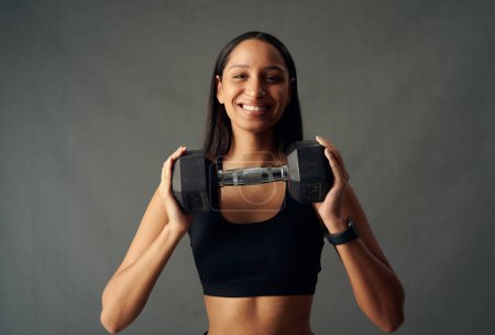 Téléchargez les photos : Portrait of young biracial woman wearing sports bra smiling while holding weights in studio - en image libre de droit