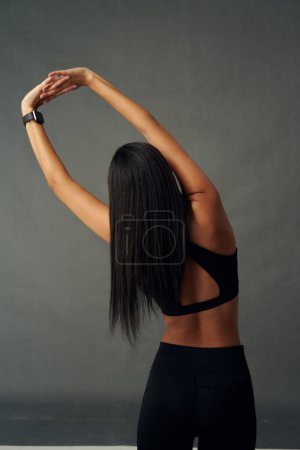 Foto de Rear view of young biracial woman wearing sports clothing while stretching with arms raised in studio - Imagen libre de derechos