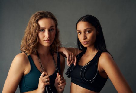 Photo for Young woman wearing sports bra holding jump rope while looking at camera with friend - Royalty Free Image
