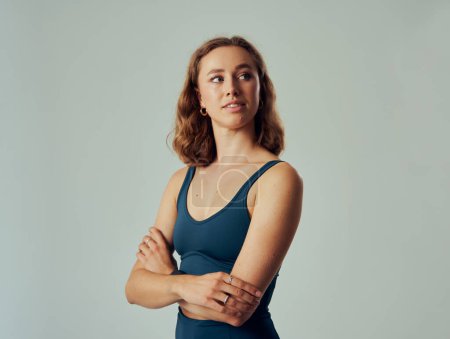 Photo for Young caucasian woman wearing sports bra looking over shoulder with arms crossed in studio - Royalty Free Image