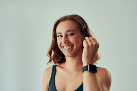 Photo for Portrait of young caucasian woman wearing fitness tracker smiling while putting in wireless headphones - Royalty Free Image