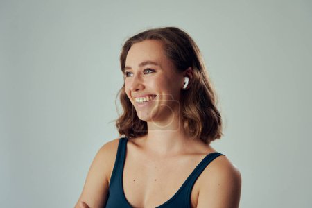 Photo for Portrait of young caucasian woman wearing sportswear smiling while using wireless in-ear headphones - Royalty Free Image