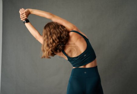 Téléchargez les photos : Rear view of young caucasian woman wearing sportswear with arms raised while stretching in studio - en image libre de droit