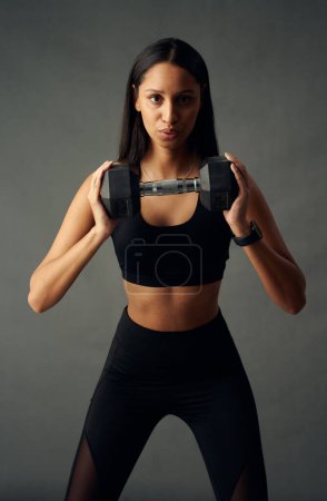 Foto de Focused young biracial woman wearing sports bra and leggings exhaling while holding weights in studio - Imagen libre de derechos