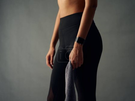 Foto de Close-up of fit biracial young woman with fitness tracker wearing leggings and holding towel in studio - Imagen libre de derechos