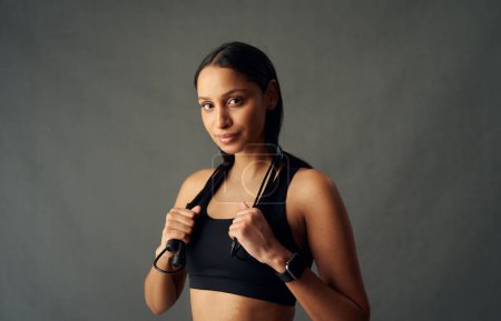 Foto de Portrait of young biracial woman wearing sports bra holding jump rope over shoulders in studio - Imagen libre de derechos