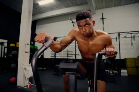 Foto de Hombre afroamericano usando un entrenador elíptico durante el entrenamiento cross fit. Entrenador personal masculino haciendo ejercicio intensamente en el gimnasio. Foto de alta calidad - Imagen libre de derechos