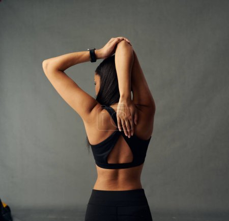 Foto de Vista trasera de una joven birracial que usa ropa deportiva con los brazos levantados estirándose en el estudio - Imagen libre de derechos