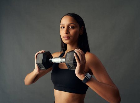 Photo for Portrait of young biracial woman wearing sports bra holding dumbbell in studio - Royalty Free Image