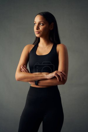 Foto de Mujer biracial joven con ropa deportiva mirando hacia otro lado con los brazos cruzados en el estudio - Imagen libre de derechos